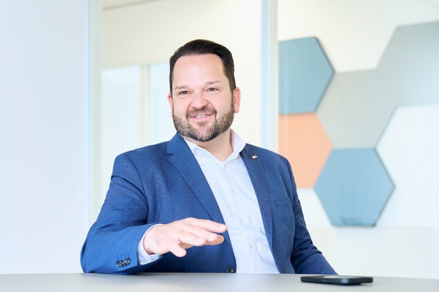 Timo Blei Mann mit Bart in formeller Kleidung, lächelt vor einem modernen Hintergrund.